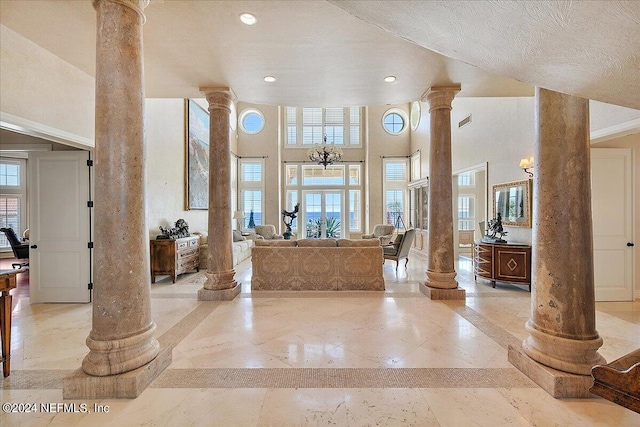 entryway featuring a notable chandelier, a wealth of natural light, a textured ceiling, and ornate columns