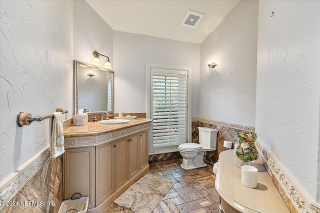 1201 Ponte Vedra Blvd, Ponte Vedra Beach, FL 32082 - bathroom featuring visible vents, stone tile flooring, vanity, toilet, and a wainscoted wall