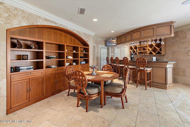 dining room with a textured ceiling, crown molding, and bar