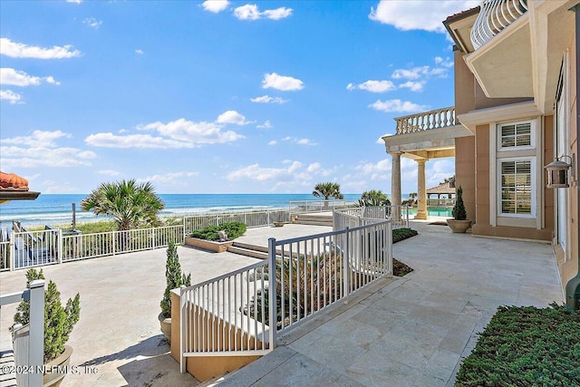 view of patio / terrace featuring a water view, a beach view, a pool, and a balcony