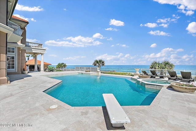 view of swimming pool with a diving board, an in ground hot tub, a water view, and a patio area