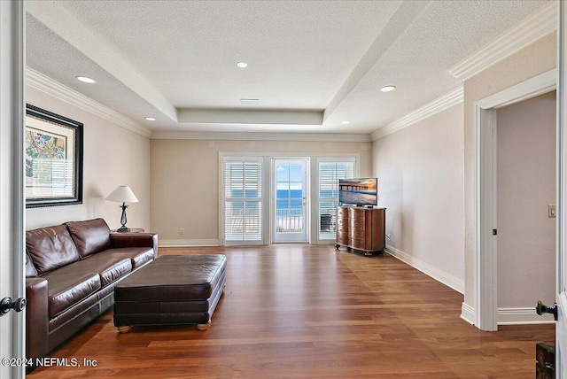 living room featuring wood-type flooring, a textured ceiling, a raised ceiling, and crown molding