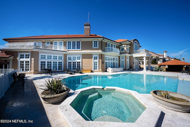 rear view of house featuring a pool with hot tub, a balcony, and a patio