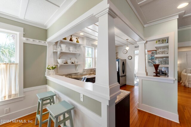 kitchen featuring hanging light fixtures, decorative columns, ornamental molding, hardwood / wood-style flooring, and stainless steel fridge