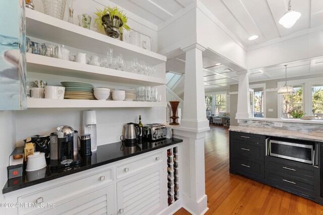 bar featuring white cabinets, light wood-type flooring, stainless steel microwave, decorative light fixtures, and ornate columns