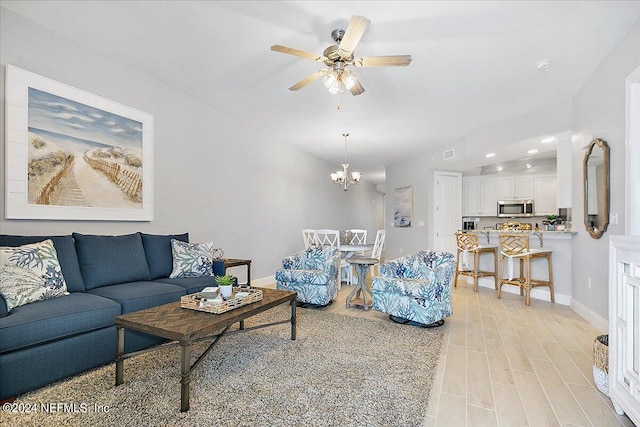 living room featuring light wood-style flooring, visible vents, baseboards, and ceiling fan with notable chandelier