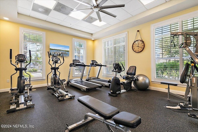 gym with a ceiling fan, a paneled ceiling, a tray ceiling, and baseboards