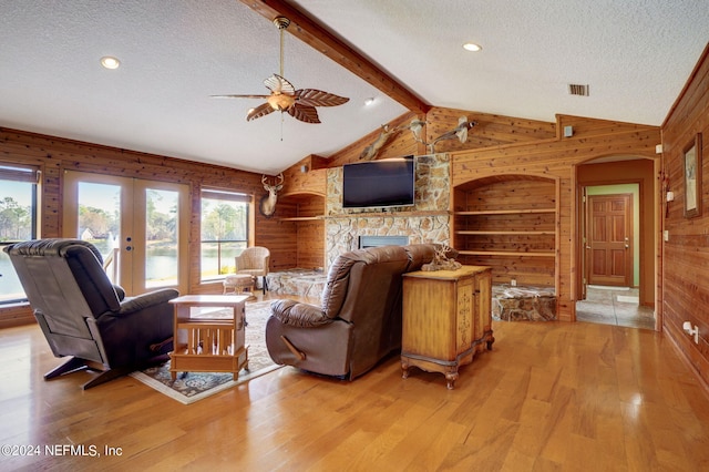 living room featuring a fireplace, built in shelves, light wood-type flooring, lofted ceiling with beams, and wooden walls