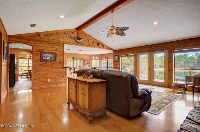 living room with french doors, light hardwood / wood-style floors, wood walls, a textured ceiling, and vaulted ceiling with beams