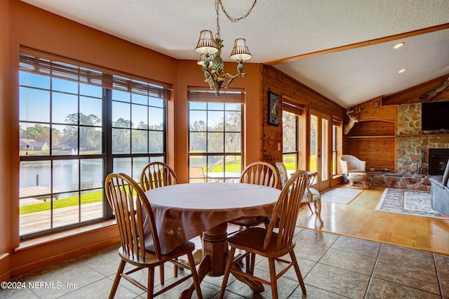 tiled dining area with a notable chandelier, a water view, wooden walls, a fireplace, and vaulted ceiling