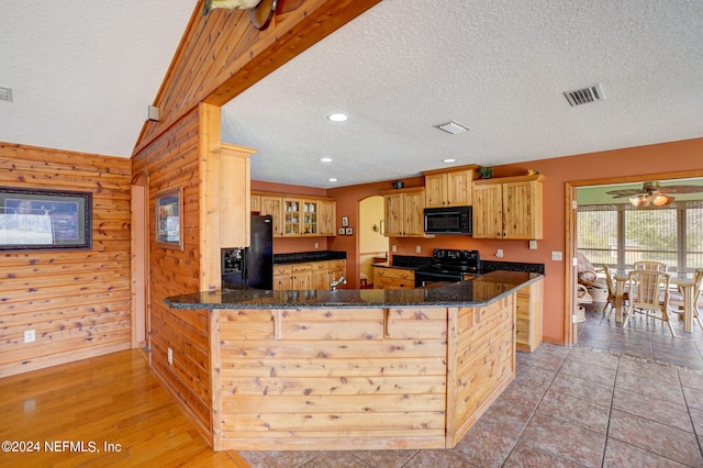 kitchen with wood walls, vaulted ceiling with beams, kitchen peninsula, light hardwood / wood-style flooring, and black appliances