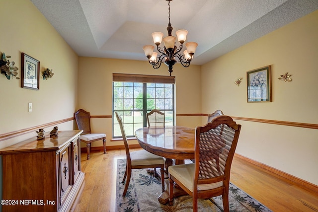 dining space featuring a textured ceiling, a chandelier, light wood-type flooring, and a tray ceiling