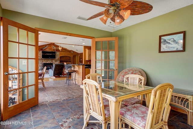 dining space with dark tile flooring, a large fireplace, a textured ceiling, and ceiling fan