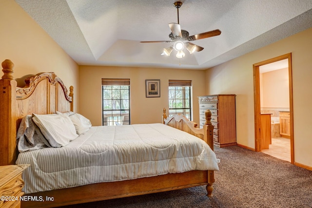 bedroom with ensuite bath, a textured ceiling, ceiling fan, and a tray ceiling