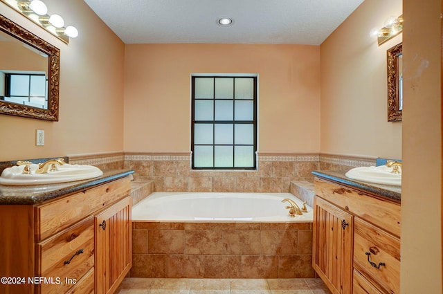 bathroom with a relaxing tiled bath, tile flooring, vanity with extensive cabinet space, double sink, and a textured ceiling