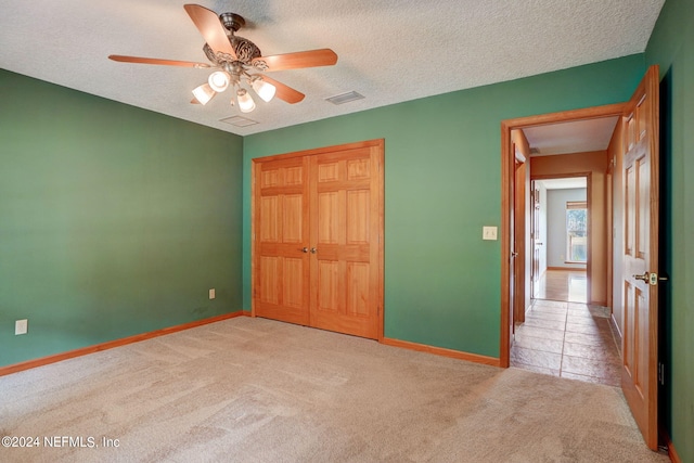 unfurnished bedroom with light carpet, a textured ceiling, a closet, and ceiling fan