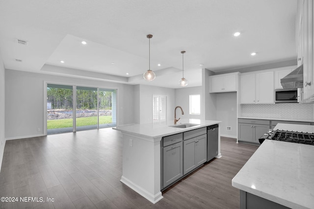 kitchen with appliances with stainless steel finishes, a raised ceiling, a kitchen island with sink, sink, and hanging light fixtures