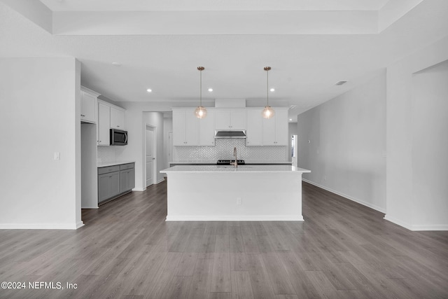 kitchen with backsplash, a center island with sink, light hardwood / wood-style flooring, white cabinetry, and hanging light fixtures