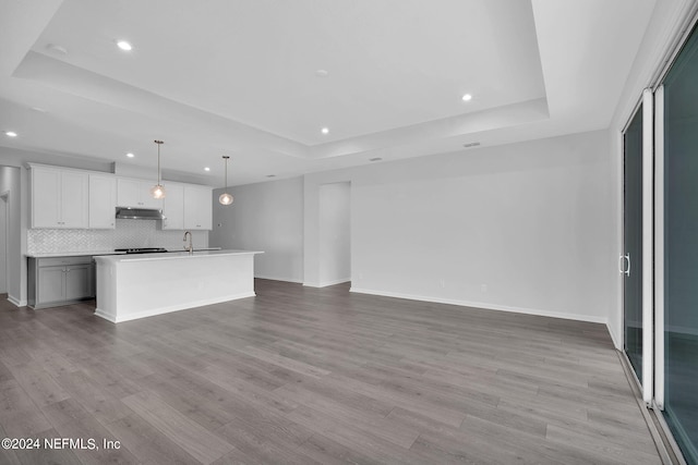 kitchen with a center island with sink, pendant lighting, white cabinets, and a tray ceiling