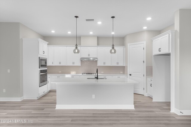 kitchen with light wood-type flooring, appliances with stainless steel finishes, a kitchen island with sink, and white cabinetry