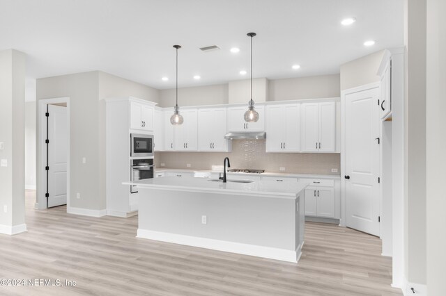 kitchen with a center island with sink, appliances with stainless steel finishes, hanging light fixtures, light hardwood / wood-style floors, and white cabinetry