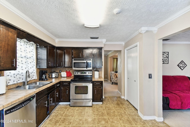 kitchen with ornamental molding, a textured ceiling, dark brown cabinetry, stainless steel appliances, and sink