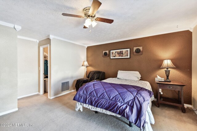 carpeted bedroom with ceiling fan, a walk in closet, ornamental molding, and a textured ceiling