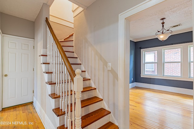 staircase featuring a textured ceiling, ornamental molding, and light hardwood / wood-style flooring