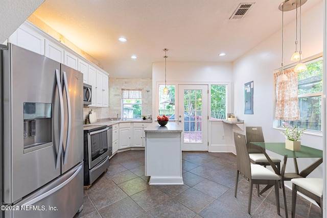 kitchen with hanging light fixtures, white cabinets, a kitchen island, and appliances with stainless steel finishes