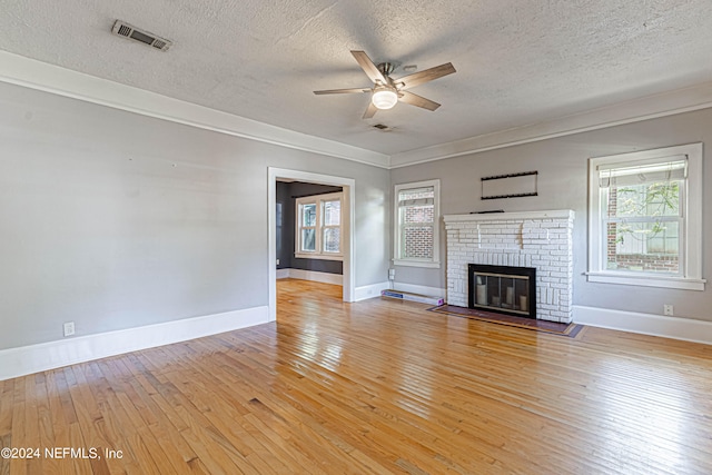 unfurnished living room with a textured ceiling, ceiling fan, a fireplace, and light wood-type flooring