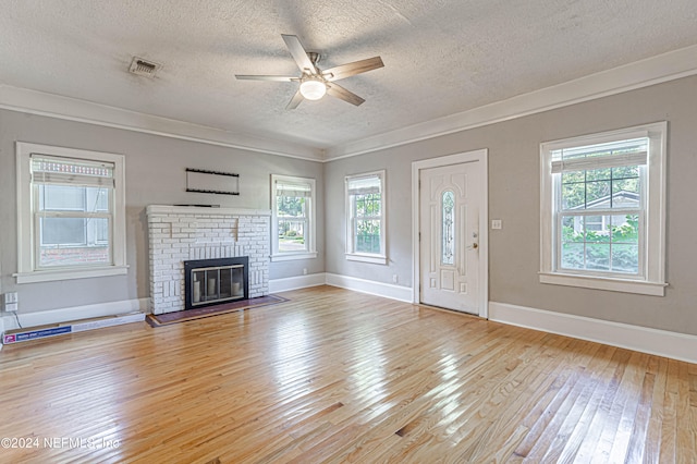 unfurnished living room featuring ceiling fan, a brick fireplace, a textured ceiling, and light hardwood / wood-style flooring