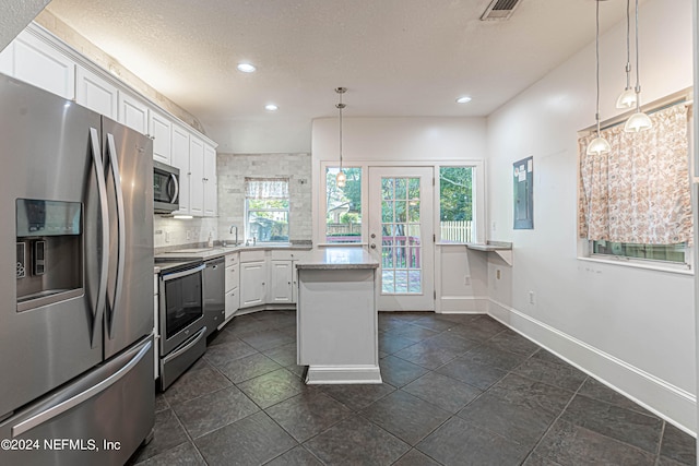 kitchen with hanging light fixtures, white cabinets, dark tile flooring, and stainless steel appliances