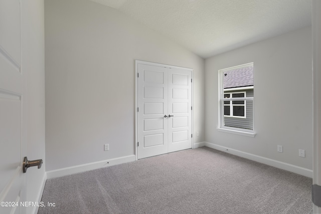 unfurnished bedroom featuring carpet flooring, lofted ceiling, a textured ceiling, and a closet