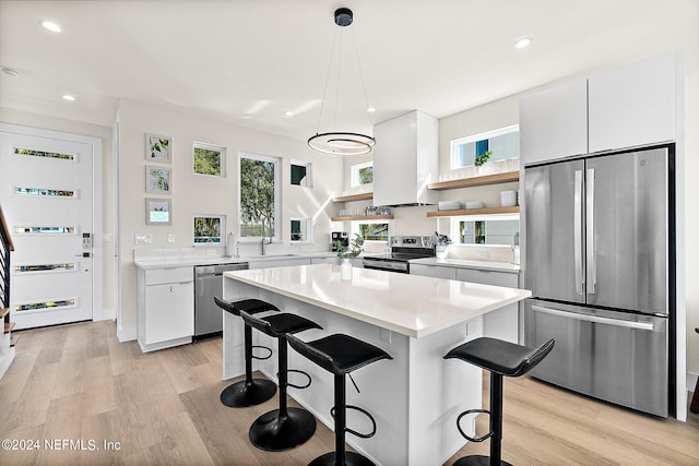 kitchen featuring white cabinetry, a kitchen breakfast bar, appliances with stainless steel finishes, light hardwood / wood-style flooring, and pendant lighting