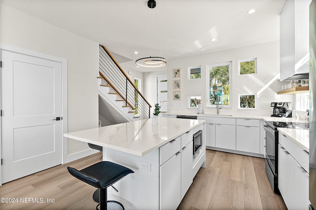 kitchen featuring light wood-type flooring, a kitchen island, electric range oven, and white cabinetry