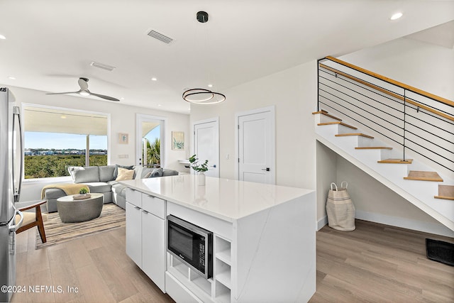 kitchen with ceiling fan, light stone counters, white cabinets, appliances with stainless steel finishes, and light hardwood / wood-style floors