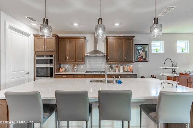 kitchen featuring an island with sink, wall chimney exhaust hood, tasteful backsplash, and stainless steel appliances