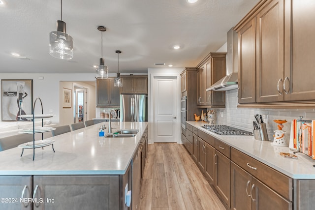 kitchen featuring a kitchen island with sink, appliances with stainless steel finishes, sink, light hardwood / wood-style flooring, and wall chimney exhaust hood