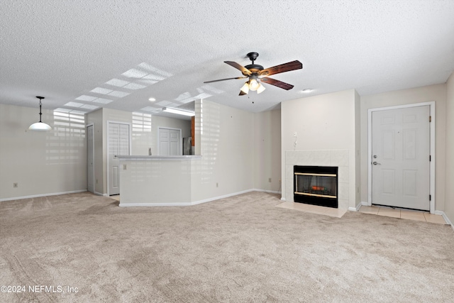 unfurnished living room with ceiling fan, light colored carpet, a textured ceiling, and a tiled fireplace