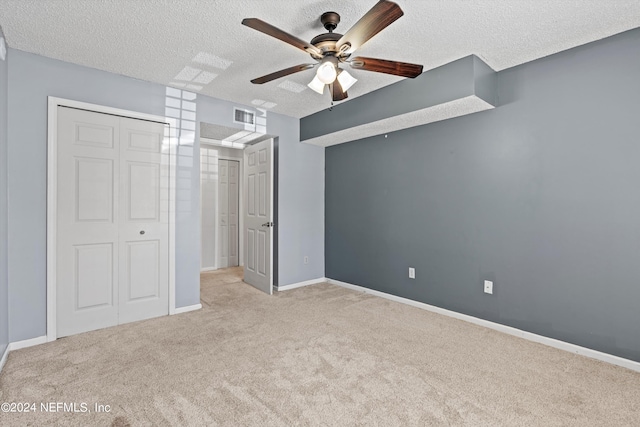 unfurnished bedroom with ceiling fan, a closet, light colored carpet, and a textured ceiling