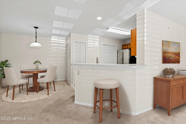 kitchen with a kitchen bar, stainless steel fridge, decorative light fixtures, and light colored carpet