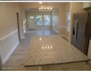 kitchen featuring pendant lighting, a center island, an inviting chandelier, stainless steel refrigerator with ice dispenser, and light stone counters