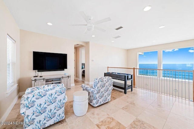 tiled living room with ceiling fan, a water view, and a wealth of natural light