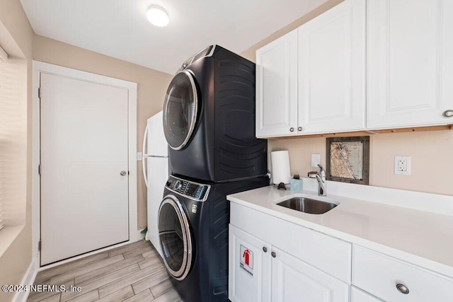 laundry area with stacked washer / drying machine, cabinets, light wood-type flooring, and sink