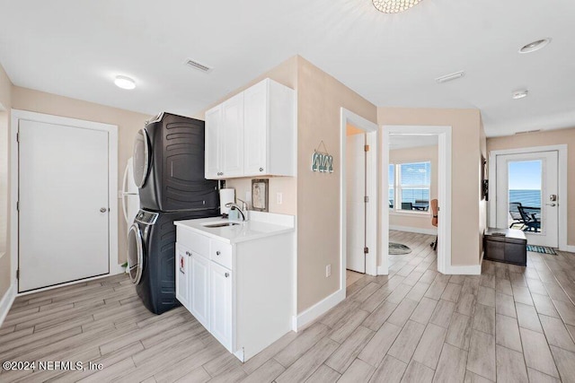 laundry room with light wood-type flooring, cabinets, and stacked washer and clothes dryer