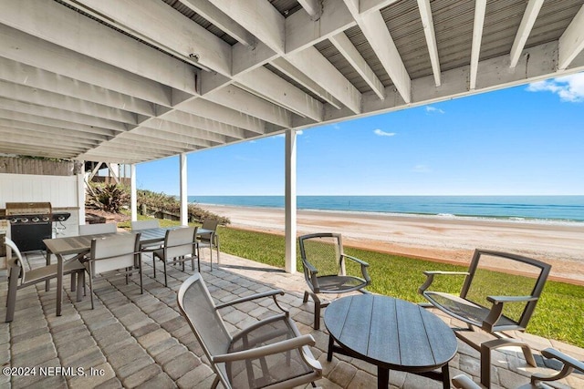 view of terrace featuring grilling area, a water view, and a view of the beach