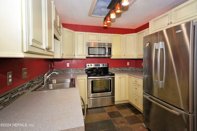 kitchen featuring cream cabinetry, sink, stainless steel appliances, and dark tile floors