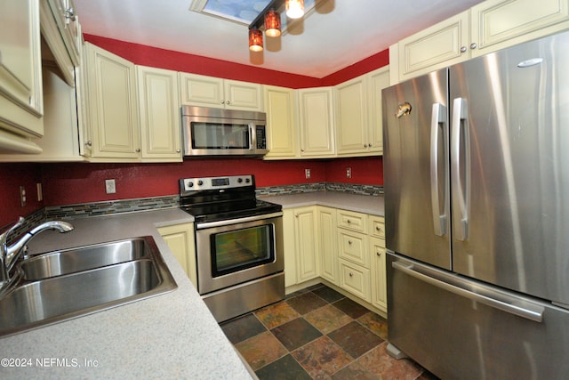 kitchen featuring appliances with stainless steel finishes, cream cabinetry, sink, and dark tile flooring