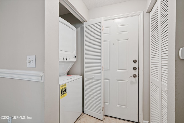 laundry area featuring a textured ceiling, light tile floors, and stacked washing maching and dryer