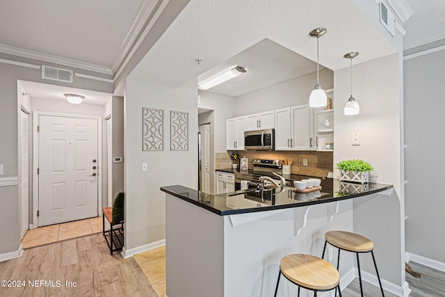 kitchen with appliances with stainless steel finishes, hanging light fixtures, light wood-type flooring, a kitchen bar, and kitchen peninsula